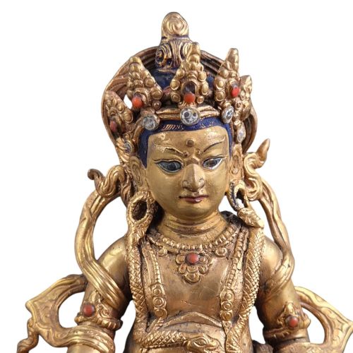 fig 1. A gilt bronze figure of the deity Jambhala crowned and adorned with jewellery, seated upon a snow lion atop an oval lotus pedestal base with red and blue painted accents.