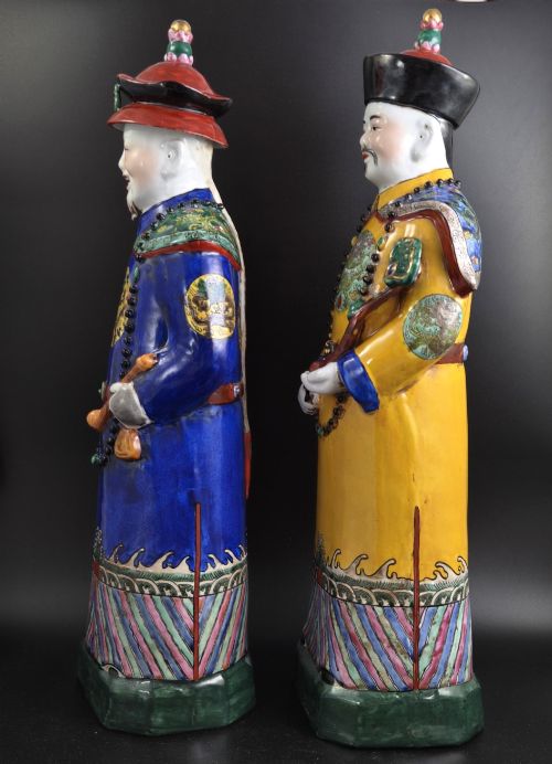fig 1. A pair of tall Chinese porcelain figures wearing traditional Qing Dynasty imperial robes in bright yellow and royal blue, adorned with dragon roundels and court beads.