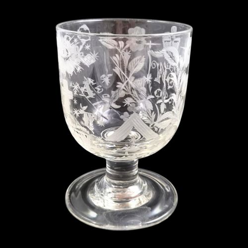 fig 1. A clear lead-glass rummer featuring detailed wheel-engraved fraternal symbols, including a central cross, all-seeing eye, crowns, and floral garlands, resting on a short stem and circular foot.