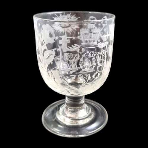 fig 3. A clear lead-glass rummer featuring detailed wheel-engraved fraternal symbols, including a central cross, all-seeing eye, crowns, and floral garlands, resting on a short stem and circular foot.