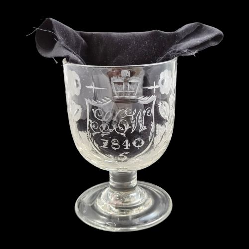 fig 6. A clear lead-glass rummer featuring detailed wheel-engraved fraternal symbols, including a central cross, all-seeing eye, crowns, and floral garlands, resting on a short stem and circular foot.