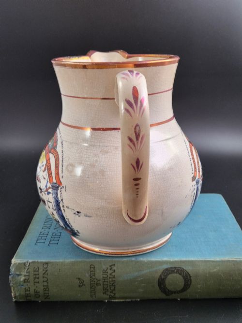 fig 3. A cream earthenware jug featuring hand-painted floral motifs, copper lustre trim, and a printed Orange Order emblematic coat of arms with religious and fraternal symbols.