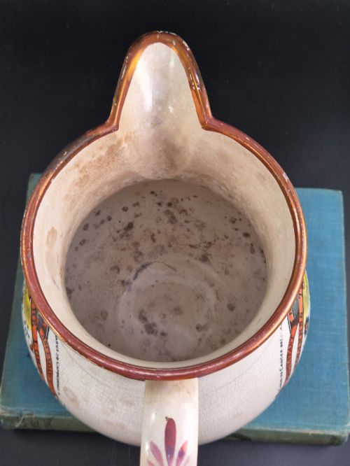 fig 4. A cream earthenware jug featuring hand-painted floral motifs, copper lustre trim, and a printed Orange Order emblematic coat of arms with religious and fraternal symbols.