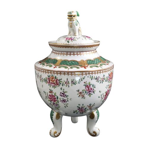 fig 2. A white hard-paste porcelain covered jar on three cabriole legs, decorated with floral enamel sprays, an armorial crest, green lattice borders, and topped with a foo dog lid finial.