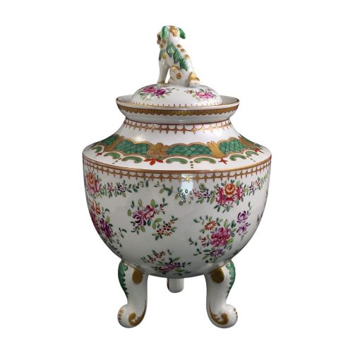fig 4. A white hard-paste porcelain covered jar on three cabriole legs, decorated with floral enamel sprays, an armorial crest, green lattice borders, and topped with a foo dog lid finial.