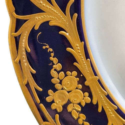 fig 2. A circular porcelain cabinet plate featuring a central hand-painted portrait of a woman framed by a deep cobalt blue rim with gold scrollwork.