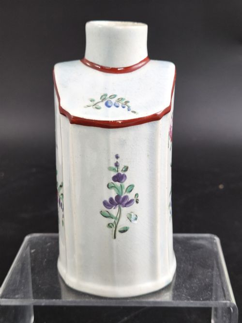 fig 1. An eighteenth-century creamware tea canister with hand-painted floral enamel motifs in purple, red, and green on an off-white earthenware body with arched reddish-brown shoulders.