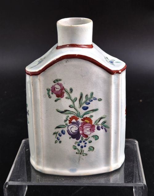 fig 2. An eighteenth-century creamware tea canister with hand-painted floral enamel motifs in purple, red, and green on an off-white earthenware body with arched reddish-brown shoulders.