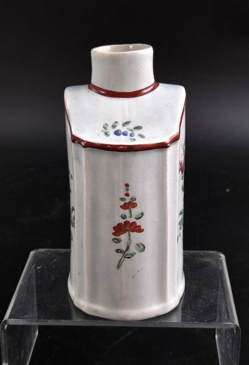 fig 3. An eighteenth-century creamware tea canister with hand-painted floral enamel motifs in purple, red, and green on an off-white earthenware body with arched reddish-brown shoulders.