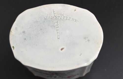 fig 5. An eighteenth-century creamware tea canister with hand-painted floral enamel motifs in purple, red, and green on an off-white earthenware body with arched reddish-brown shoulders.