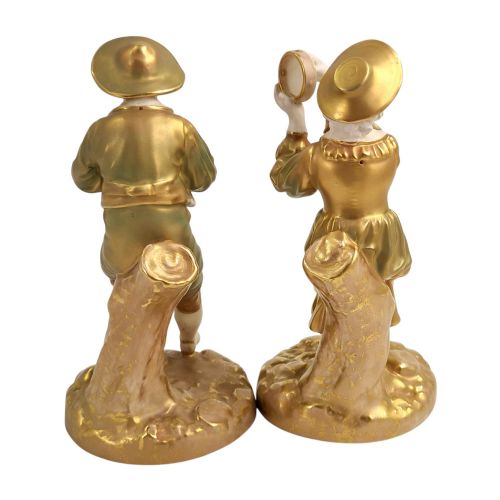 fig 2. A pair of mid-century Royal Worcester bone china figurines depicting Strephon playing a pipe instrument and Phyllis playing a tambourine, finished in metallic gold and off-white porcelain.