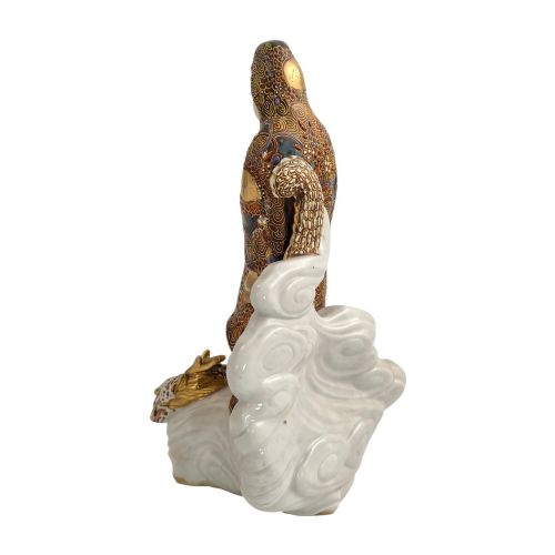 fig 3. A Japanese Kutani porcelain figure of the deity Kannon in detailed patterned robes, standing atop a white sea dragon amidst sculpted waves.