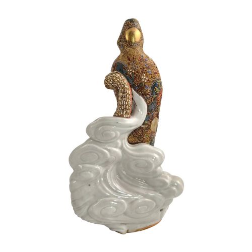 fig 4. A Japanese Kutani porcelain figure of the deity Kannon in detailed patterned robes, standing atop a white sea dragon amidst sculpted waves.