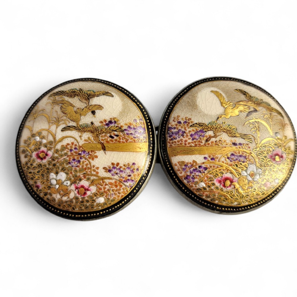 A pair of circular Japanese Kyo-Satsuma belt buckle halves set in silver frames, decorated with intricate hand-painted birds and flowers on a cream crackle-glazed background.
