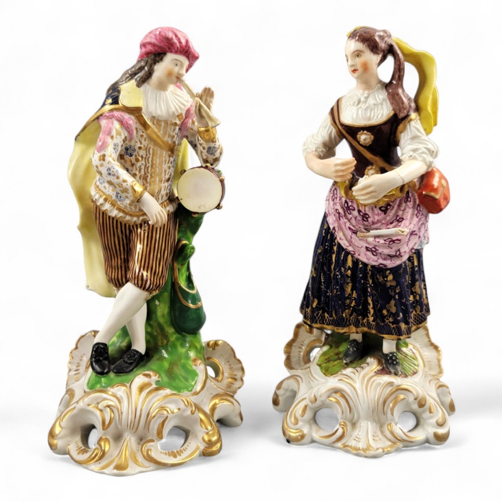 A pair of 19th-century Bloor Derby porcelain figurines depicting a male and female musician in colourful costume on gilded rocaille bases.