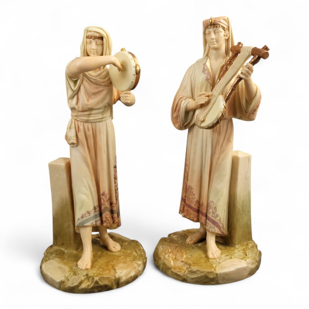 A pair of Victorian Royal Worcester porcelain figures depicting Egyptian musicians with detailed draped robes and musical instruments on naturalistic bases.