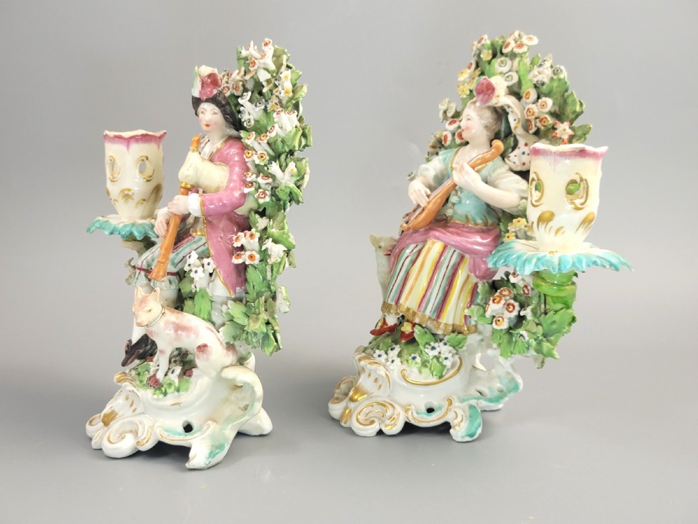A pair of 18th-century soft-paste Derby porcelain candlesticks depicting a male and female musician seated before leafy floral bocage backdrops. View II