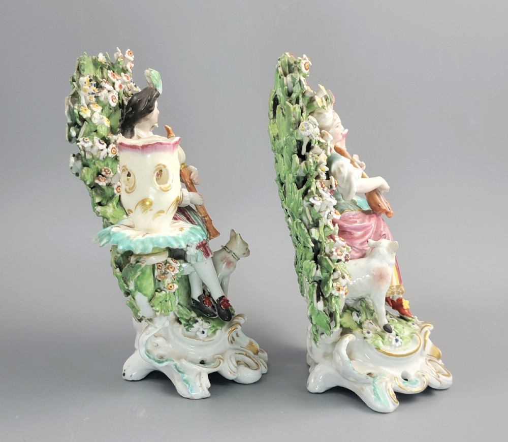 A pair of 18th-century soft-paste Derby porcelain candlesticks depicting a male and female musician seated before leafy floral bocage backdrops. View IV