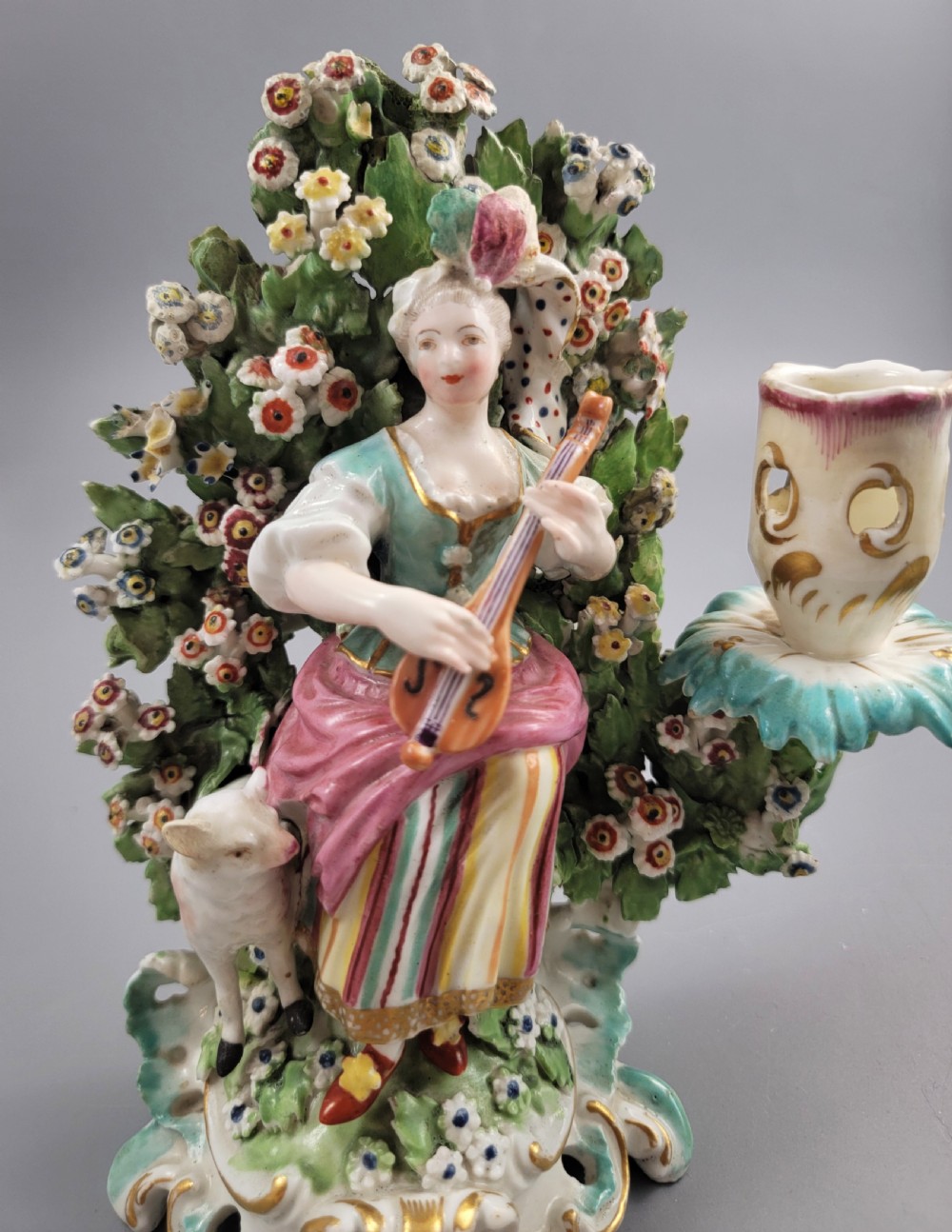 A pair of 18th-century soft-paste Derby porcelain candlesticks depicting a male and female musician seated before leafy floral bocage backdrops. View VIII
