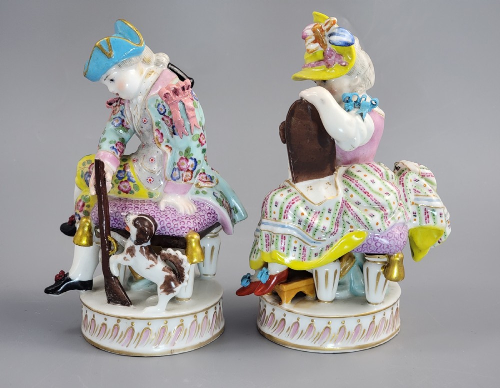 A pair of 18th-century hand-painted Meissen porcelain figurines depicting a boy and girl seated on stools with small dogs on circular fluted bases. View II
