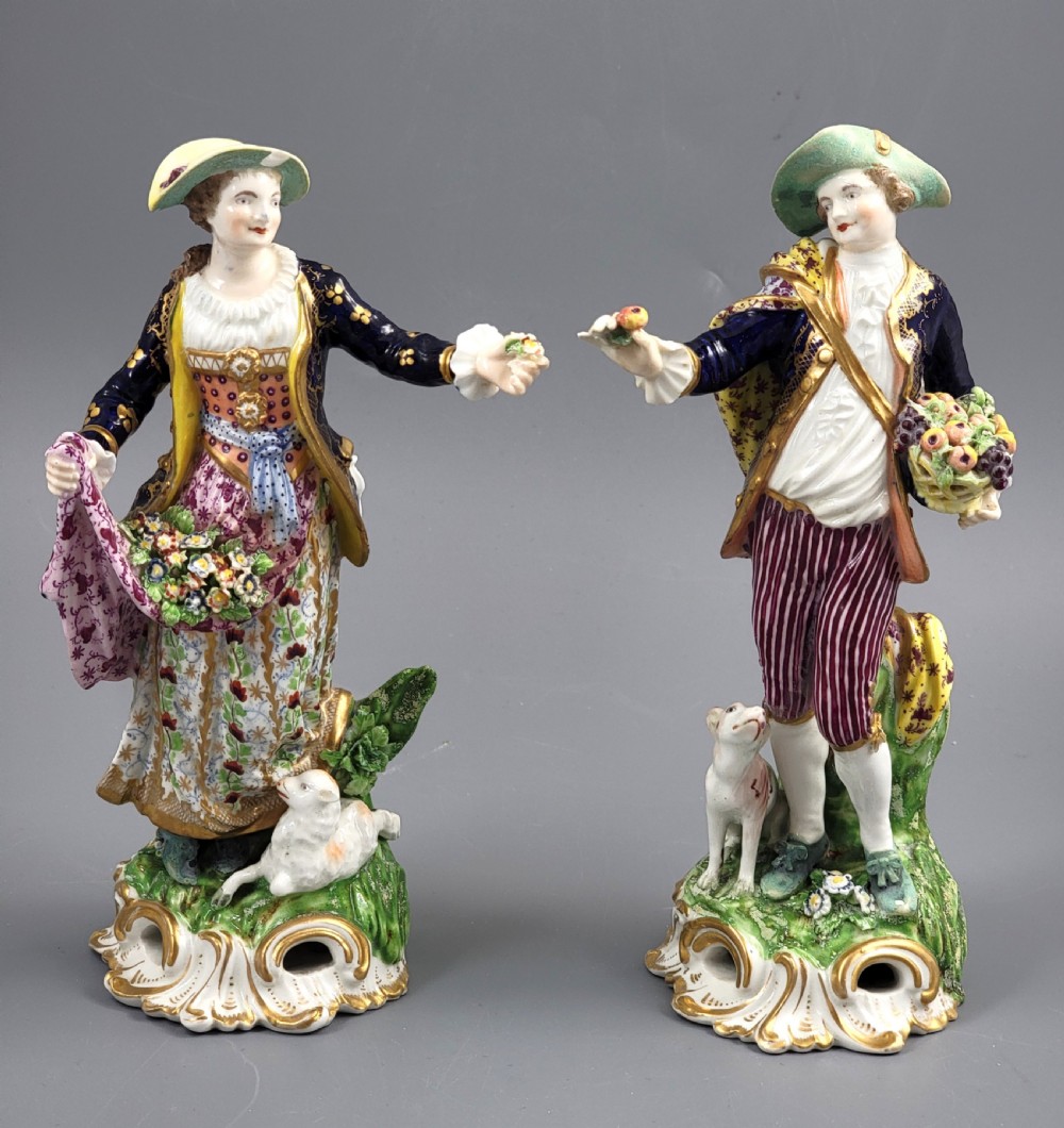 A pair of 19th-century Bloor Derby porcelain figurines depicting a shepherdess with a lamb and a shepherd with a dog, painted in multi-coloured enamels with gilded Rococo scroll bases.