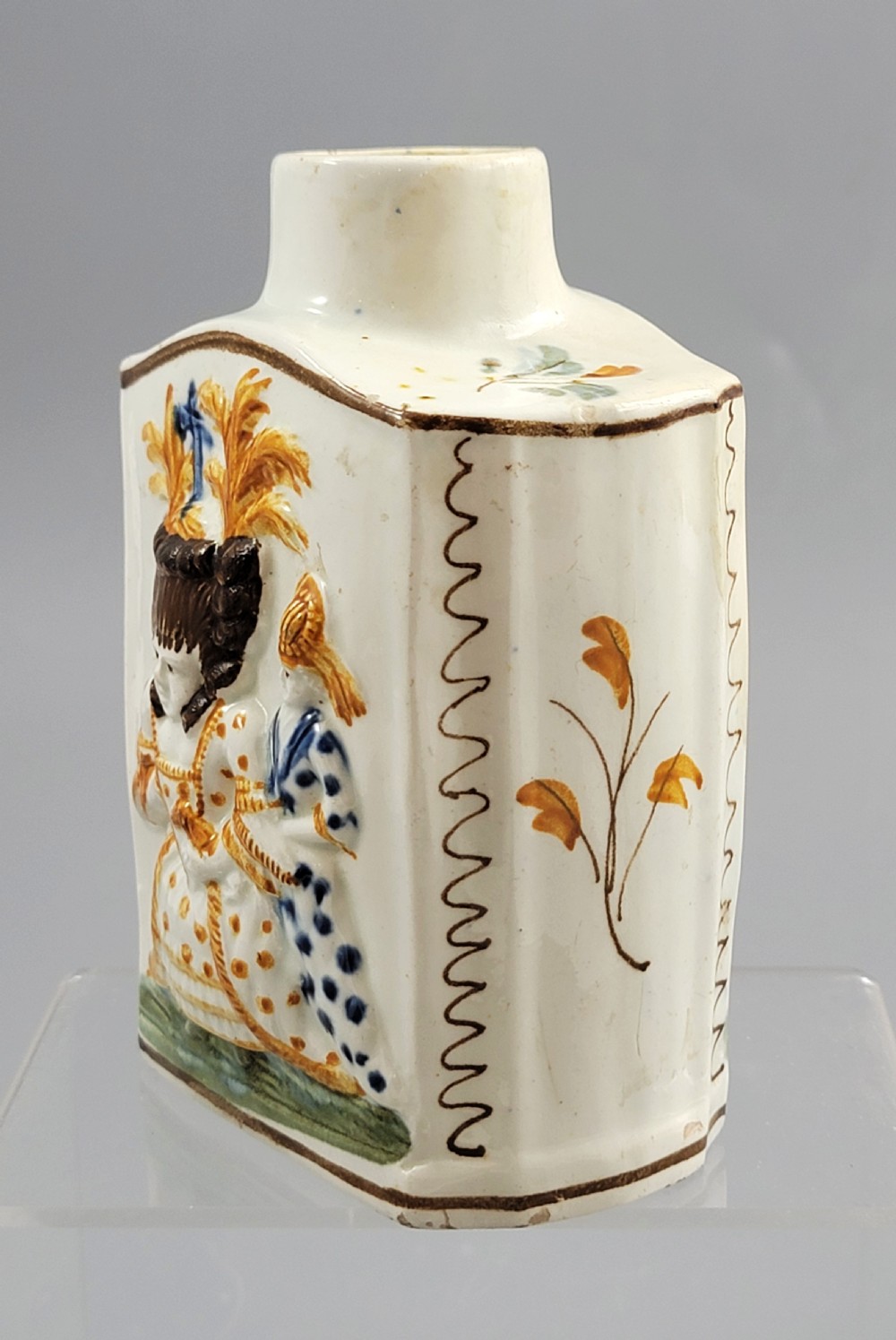 A late 18th-century cream-coloured pearlware tea caddy featuring moulded relief figures painted in ochre and cobalt blue glazes. View II