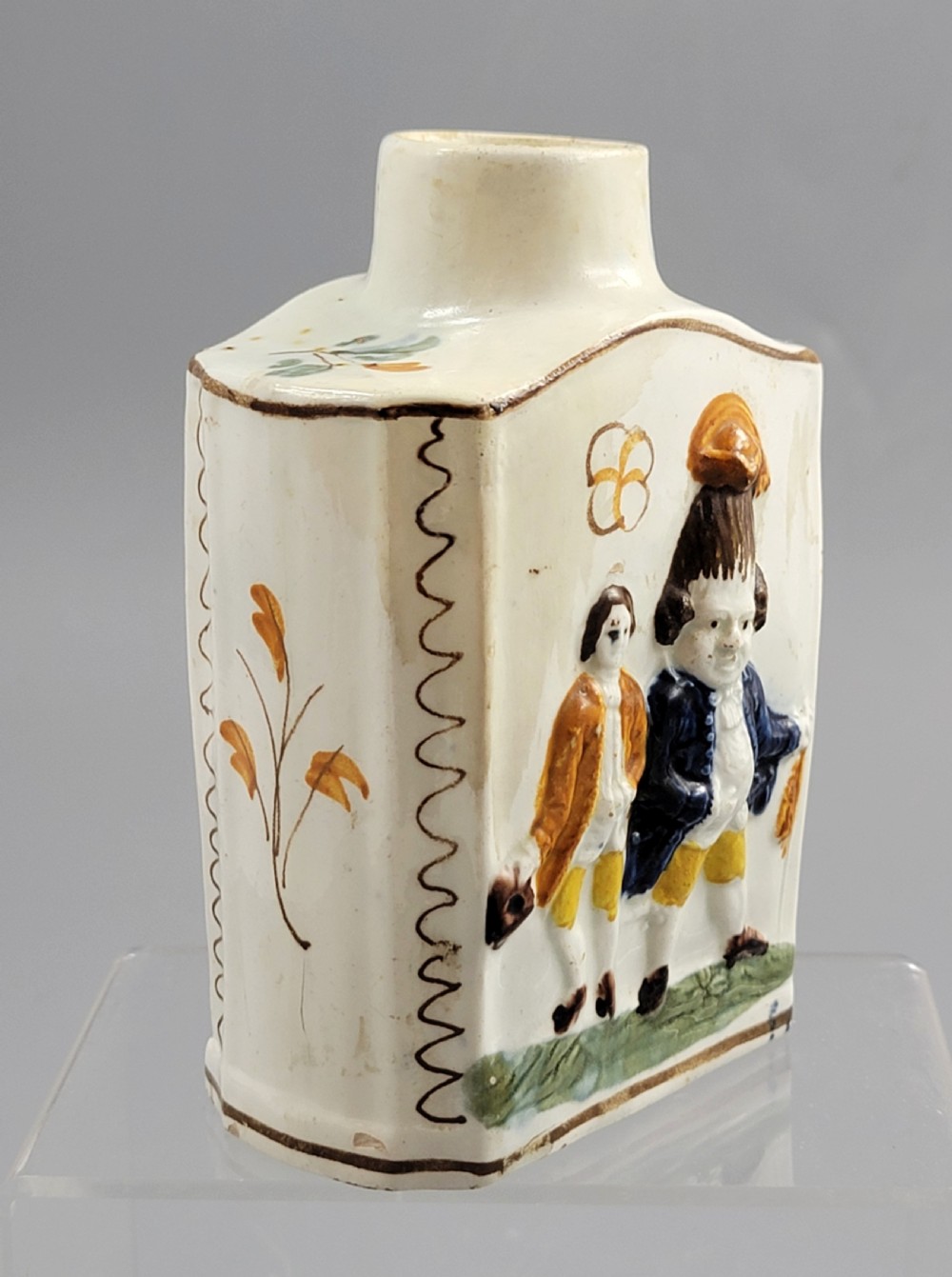 A late 18th-century cream-coloured pearlware tea caddy featuring moulded relief figures painted in ochre and cobalt blue glazes. View IV