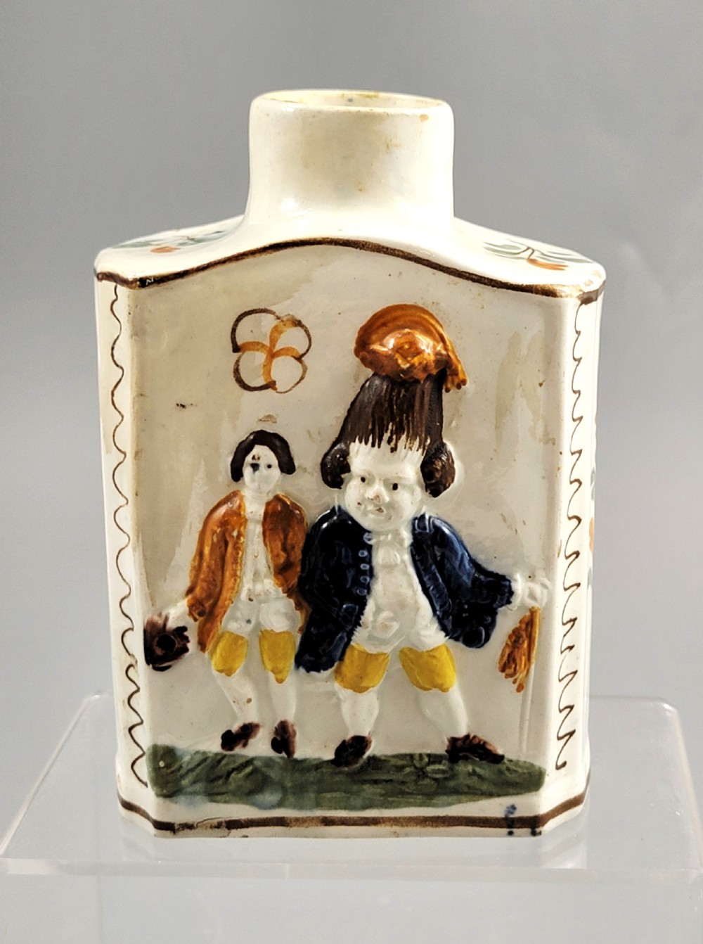 A late 18th-century cream-coloured pearlware tea caddy featuring moulded relief figures painted in ochre and cobalt blue glazes. View V