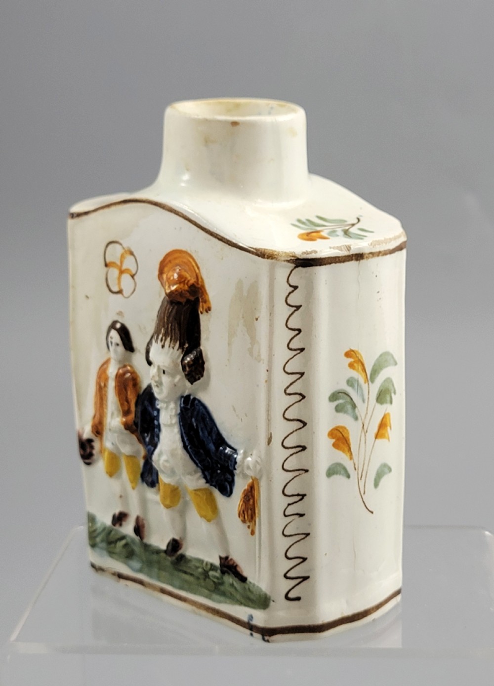 A late 18th-century cream-coloured pearlware tea caddy featuring moulded relief figures painted in ochre and cobalt blue glazes. View VI