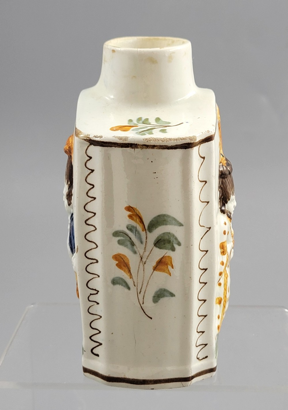 A late 18th-century cream-coloured pearlware tea caddy featuring moulded relief figures painted in ochre and cobalt blue glazes. View VII