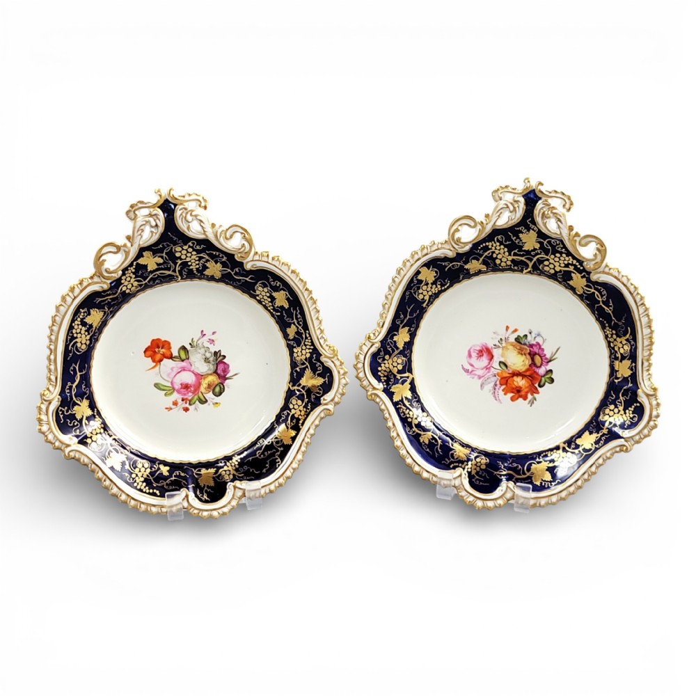 A pair of shaped English porcelain serving dishes featuring cobalt blue rims with gilded foliage patterns and hand-painted central floral bouquets.