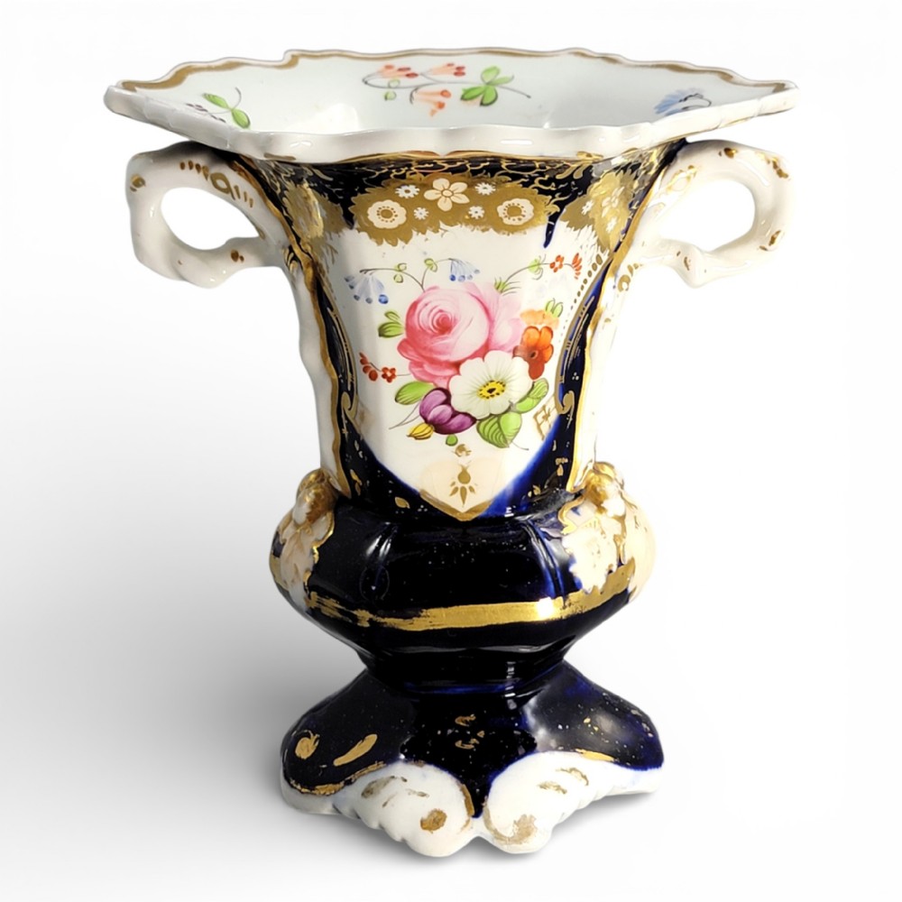 An early nineteenth-century French porcelain vase featuring hand-painted pink floral motifs, cobalt blue glaze, twin scroll handles, and gold leaf embellishments.
