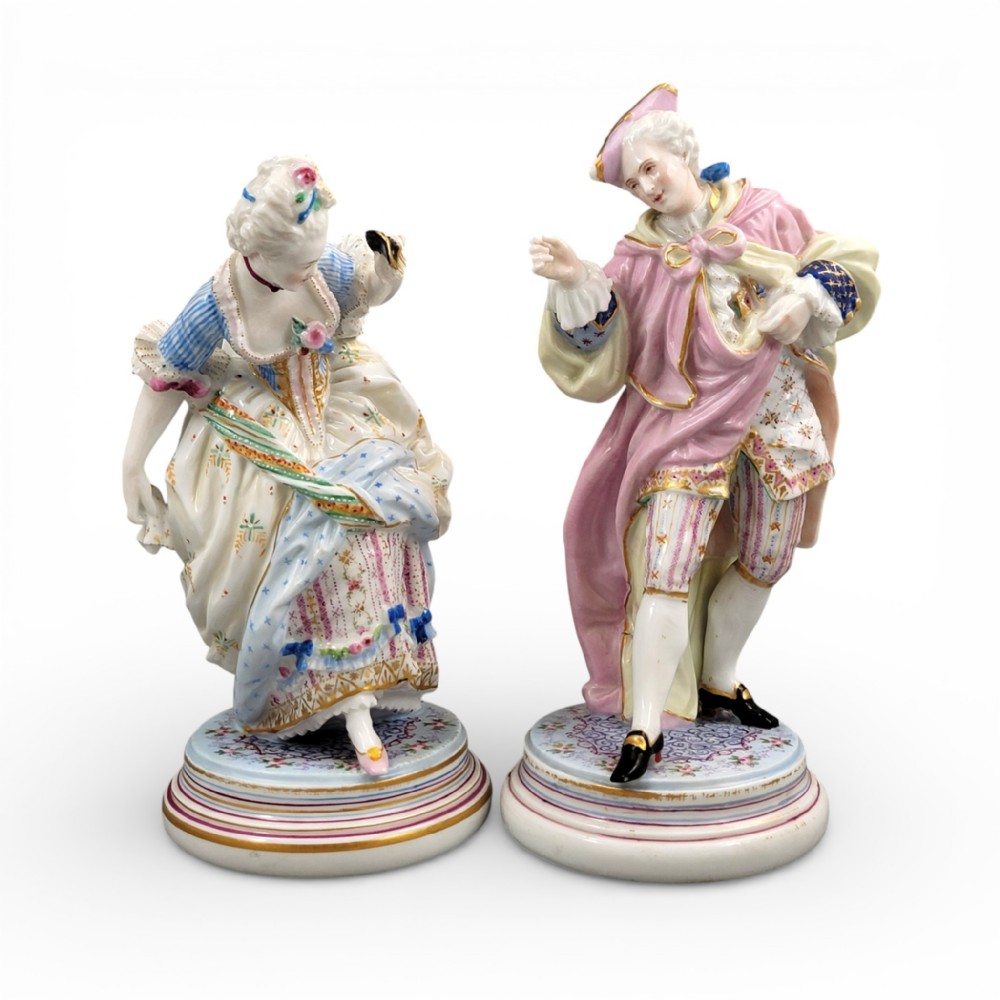 Pair of hand-painted French Paris porcelain masquerade figures depicting a lady and gallant in pastel eighteenth-century costume on gilded circular bases.