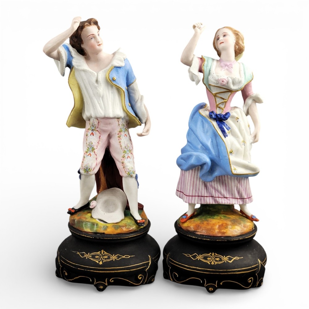 A pair of 19th-century French porcelain figurines featuring a man and woman in 18th-century style attire on black painted bases.