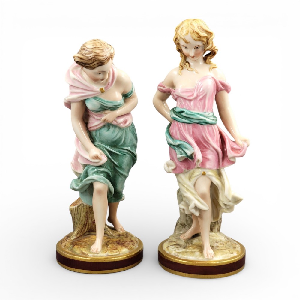 A pair of Victorian Royal Worcester porcelain figures depicting draped maidens with pink and green dresses standing on circular bases.