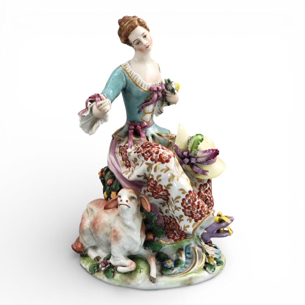 A Samson Paris hand-painted porcelain figurine depicting a seated shepherdess with a floral skirt beside a resting lamb on a floral encrusted base.