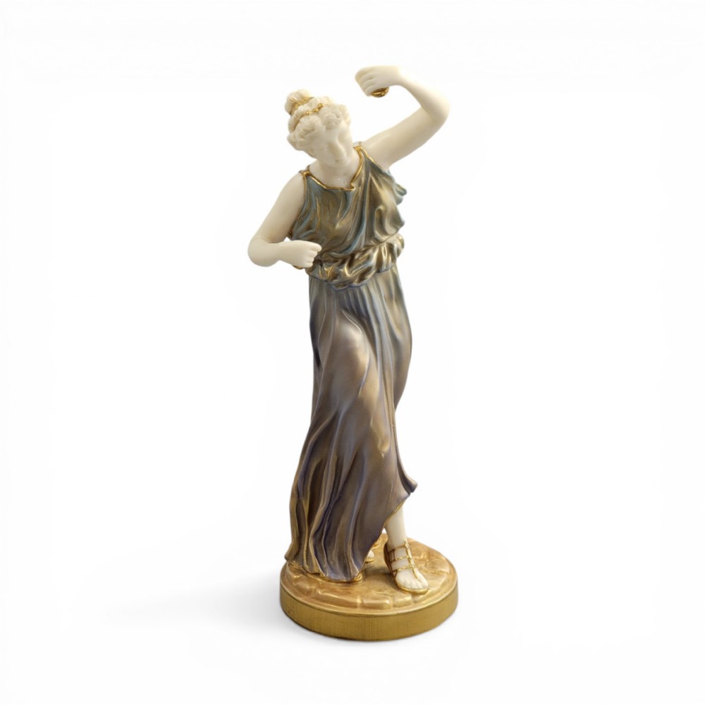 A porcelain figurine of a woman wearing classical draped robes with gilded trim standing on a circular base.