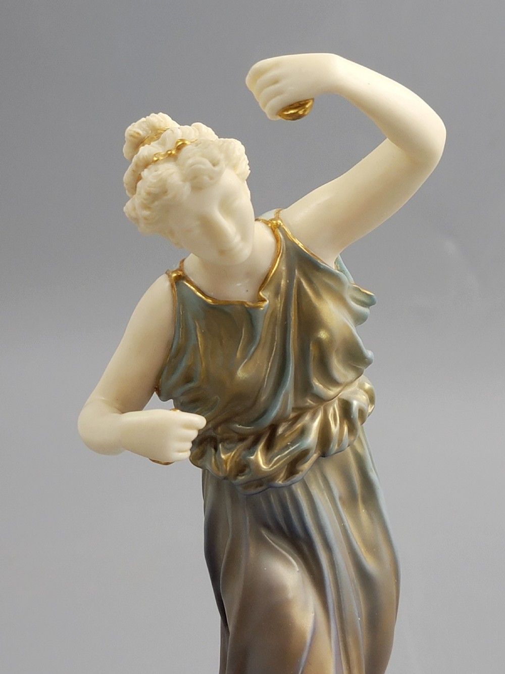 A porcelain figurine of a woman wearing classical draped robes with gilded trim standing on a circular base. View VII