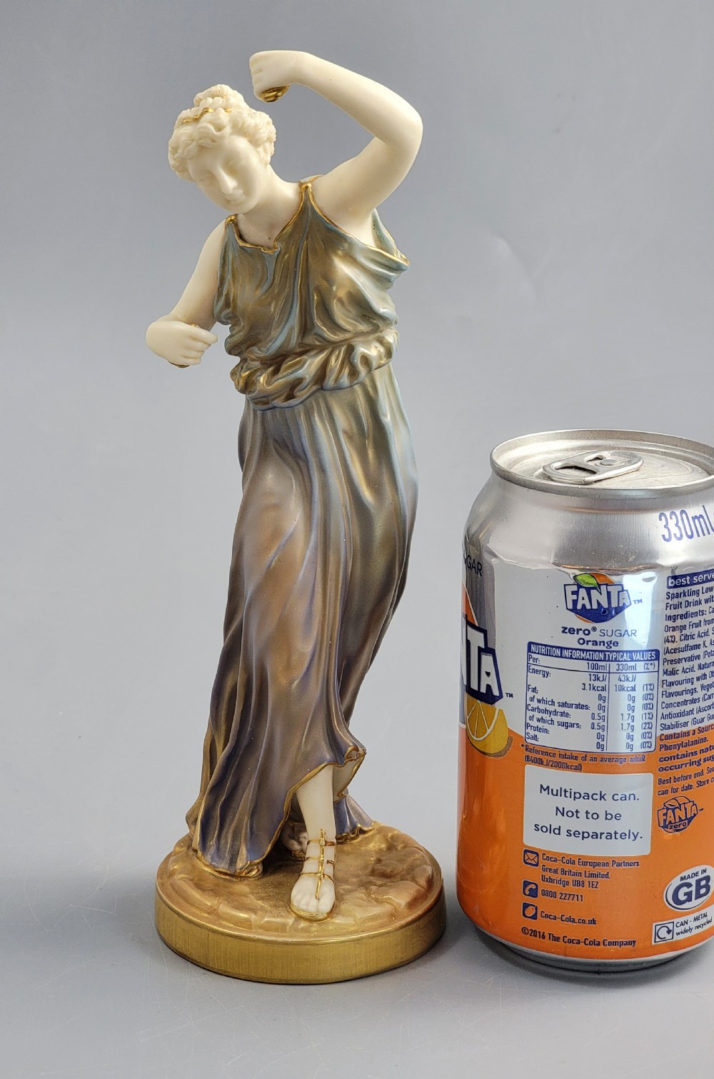 A porcelain figurine of a woman wearing classical draped robes with gilded trim standing on a circular base. View XII
