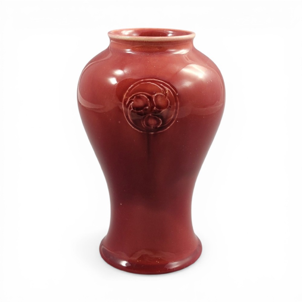 A red glazed earthenware vase featuring a baluster shape with an embossed roundel medallion near the rim.