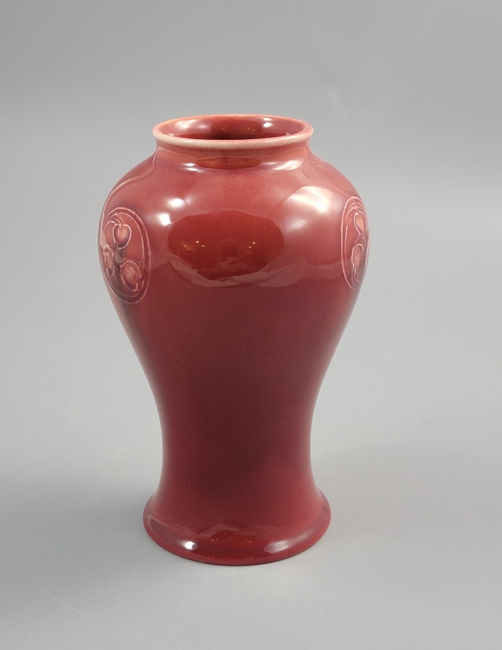 A red glazed earthenware vase featuring a baluster shape with an embossed roundel medallion near the rim. View VI