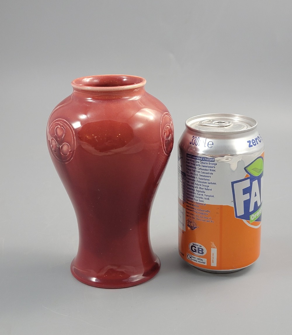 A red glazed earthenware vase featuring a baluster shape with an embossed roundel medallion near the rim. View IX