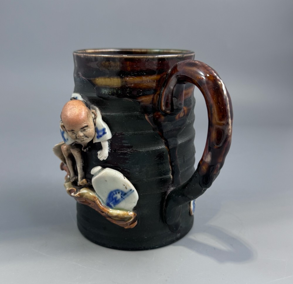 A dark ribbed ceramic mug featuring a dripping flambe glaze rim and an applied relief figure of a seated Japanese sennin. View V