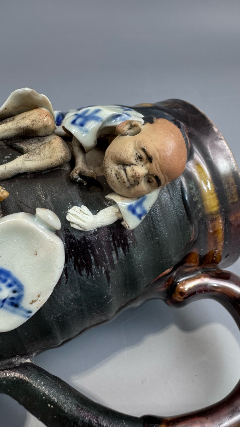 A dark ribbed ceramic mug featuring a dripping flambe glaze rim and an applied relief figure of a seated Japanese sennin. View XI