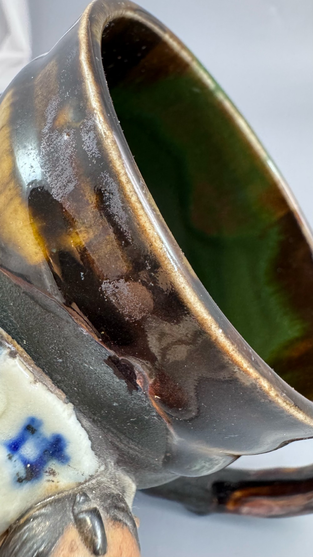 A dark ribbed ceramic mug featuring a dripping flambe glaze rim and an applied relief figure of a seated Japanese sennin. View XIV