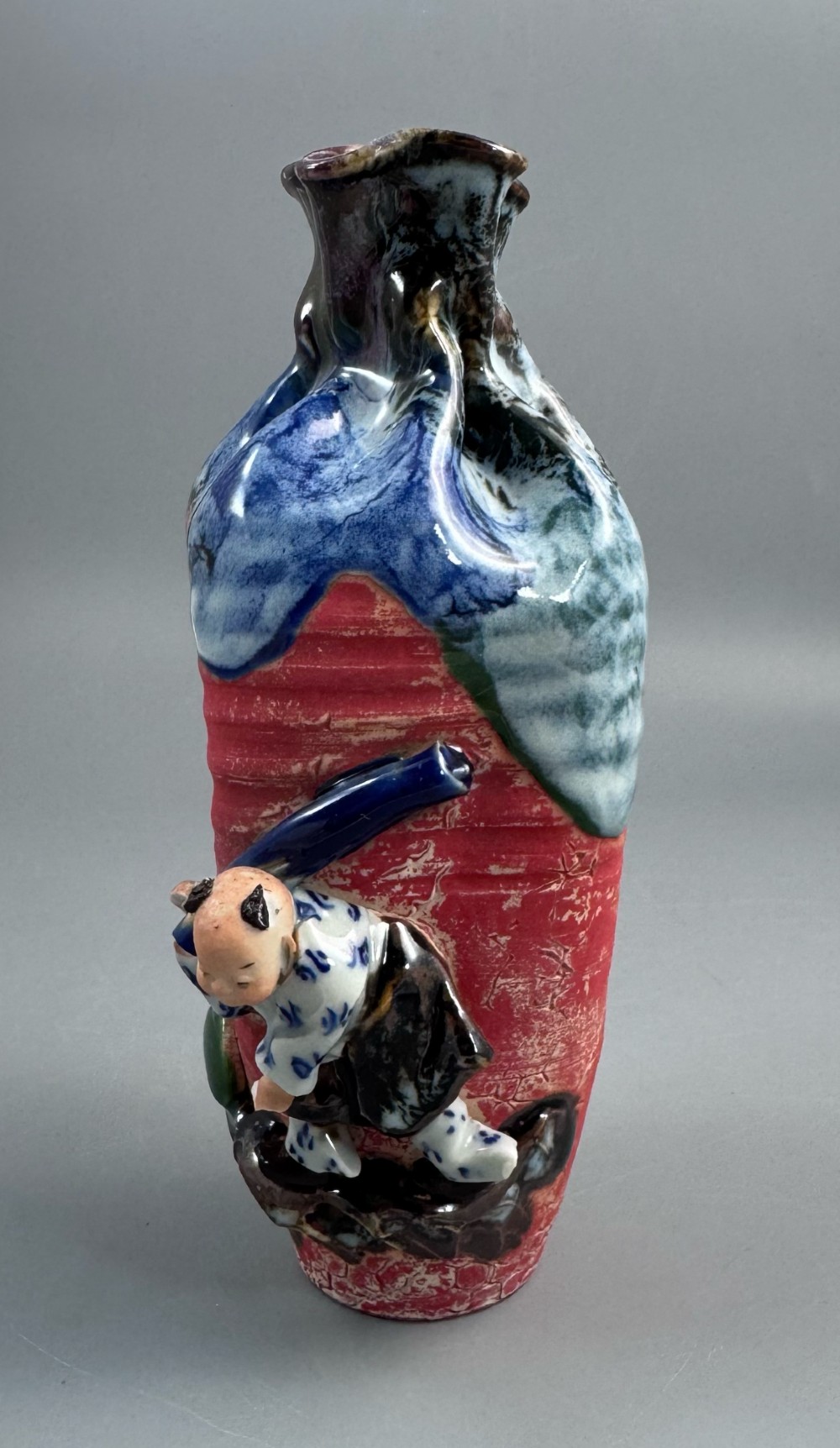 A Japanese Sumida Gawa baluster vase featuring a ribbed red surface, a dripping blue flambe glaze at the rim, and a sculpted karako figure on the side.