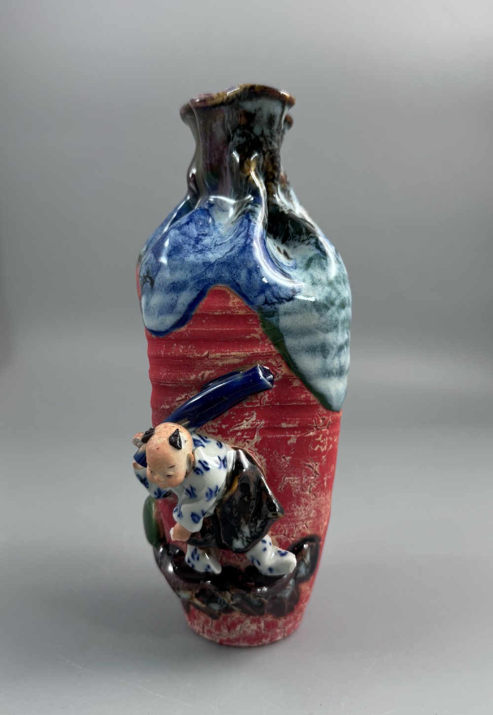 A Japanese Sumida Gawa baluster vase featuring a ribbed red surface, a dripping blue flambe glaze at the rim, and a sculpted karako figure on the side. View II