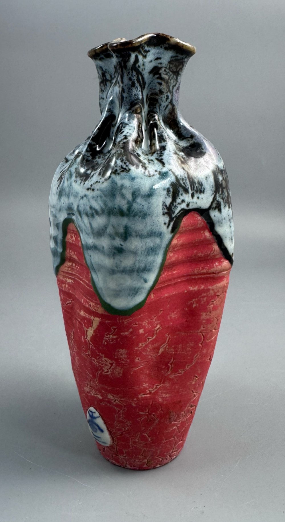 A Japanese Sumida Gawa baluster vase featuring a ribbed red surface, a dripping blue flambe glaze at the rim, and a sculpted karako figure on the side. View IV