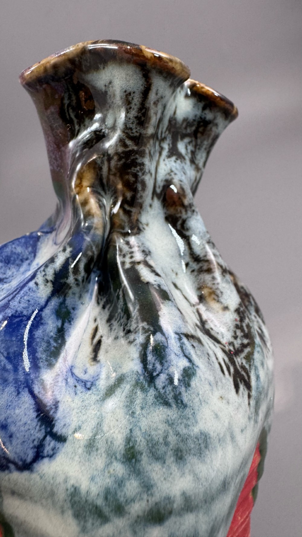 A Japanese Sumida Gawa baluster vase featuring a ribbed red surface, a dripping blue flambe glaze at the rim, and a sculpted karako figure on the side. View XII