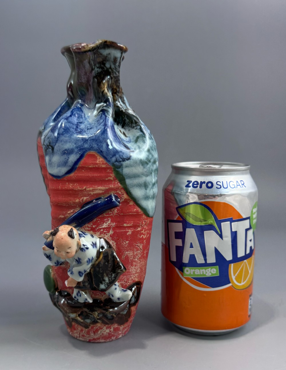 A Japanese Sumida Gawa baluster vase featuring a ribbed red surface, a dripping blue flambe glaze at the rim, and a sculpted karako figure on the side. View XIV
